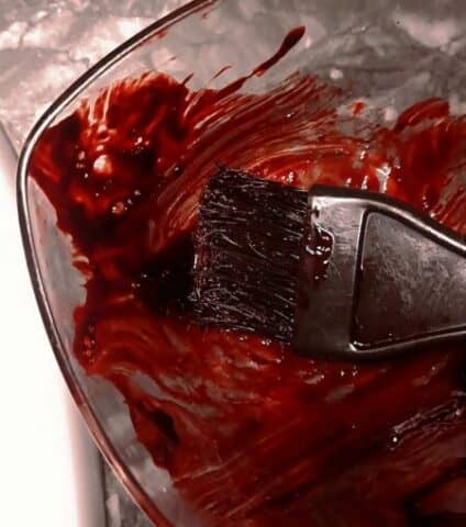 γυάλινο μπολάκι με κόκκινη βαφή μαλλιών και πινέλο βαψίματος μαλλιών πάνω σε μαρμάρινο πάγκο